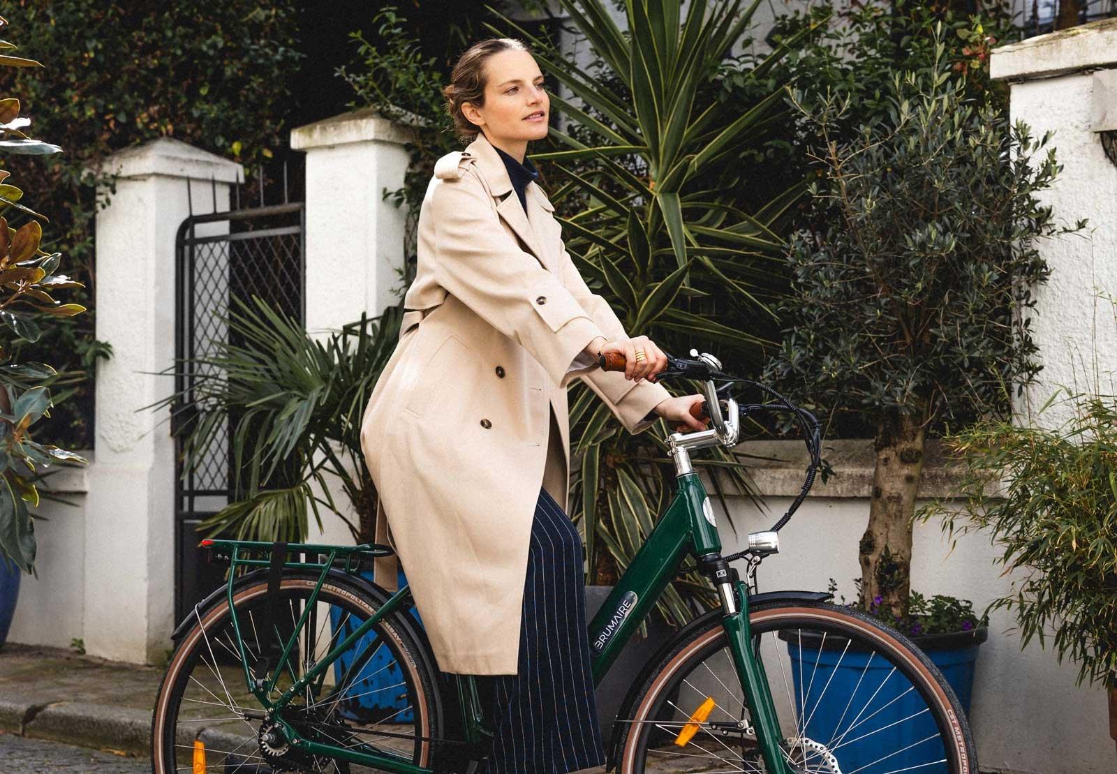 Une femme sur un vélo électrique devant une haie de maison